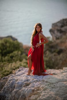 Woman sunset sea red dress, back view a happy beautiful sensual woman in a red long dress posing on a rock high above the sea on sunset