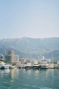 Row of yachts moored off the coast with high-rise buildings at the foot of the mountains. High quality photo