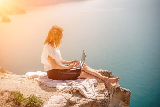 Freelance woman working on a laptop by the sea, typing away on the keyboard while enjoying the beautiful view, highlighting the idea of remote work