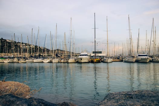 Yachts in the port, sailboats modern water transport. Beautiful moored sail yachts in the sea, modern water transport Barcelona, Catalonia. Bright sunset and dusk. High quality picture for wallpaper, article