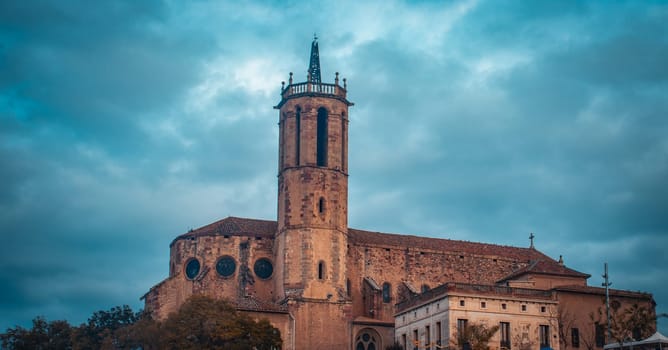 St Mary Church in Catalonia photo. Romanesque architecture in Caldes de Montbui, Barcelona Province. Street scene with dramatic morning sky. High quality picture for wallpaper, article