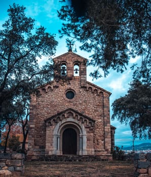 Catholic church located in Catalonia neighborhood. Red brick building surrounded by trees. Typical countryside religion building in Spain. High quality picture for wallpaper, article