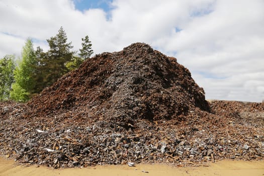 A large pile of rusty metal waste against the background of the sky and trees.