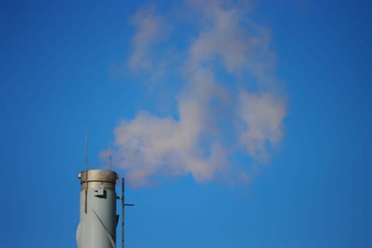 Carbon Emissions Concept. Rusty chimney. Factory smoke causes pollution in the air. Fuming chimney against blue sky.