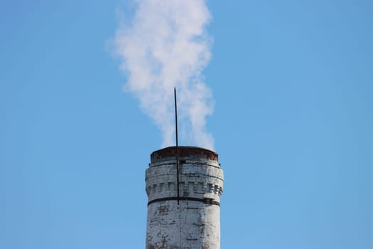 Carbon Emissions Concept. Smoke from industrial chimney. An old brick chimney with smoke against the background of a clear blue sky.