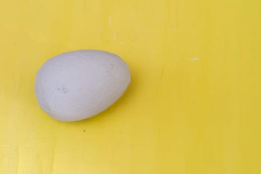 Handmade egg covered with gray plaster on a yellow background. Trendy minimalist. Minimal Easter.