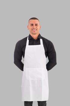 Attractive chef or waiter posing, wearing white apron and black shirt on gray background, in studio shot