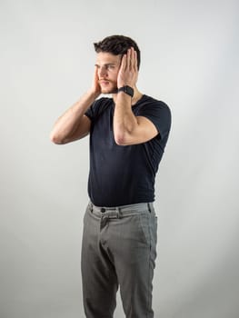 Depressed, sad or irritated young man covering ears with hands, in studio shot