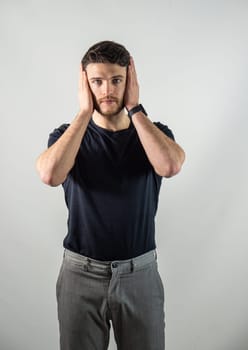 Depressed, sad or irritated young man covering ears with hands, in studio shot