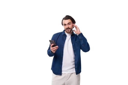 young well-groomed brunette guy in a casual blue shirt holds a mobile phone in his hands.