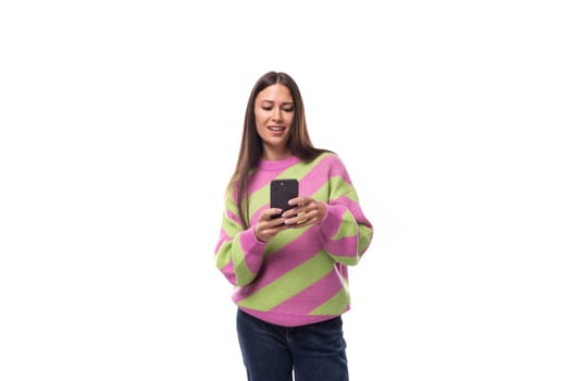 beautiful young brunette woman in a striped pink blouse communicates in social networks on a smartphone on a white background with copy space.