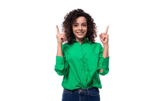 surprised young woman with black curly hair dressed in a green blouse points her fingers up.