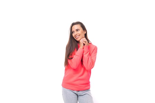 portrait of a young beautiful dreaming european model woman with long black hair dressed in a pink sweater on a white background with copy space.