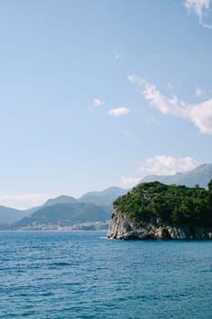 Green rocky cape in the sea against the backdrop of a mountain range. High quality photo