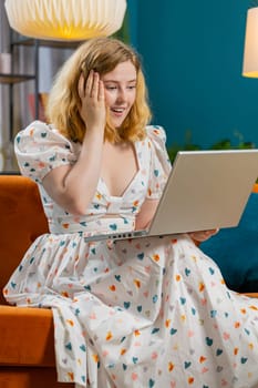 Surprised happy redhead young adult woman using laptop computer receive good news success message shocked by sudden victory celebrate lottery jackpot win purchases online shopping at home. Vertical