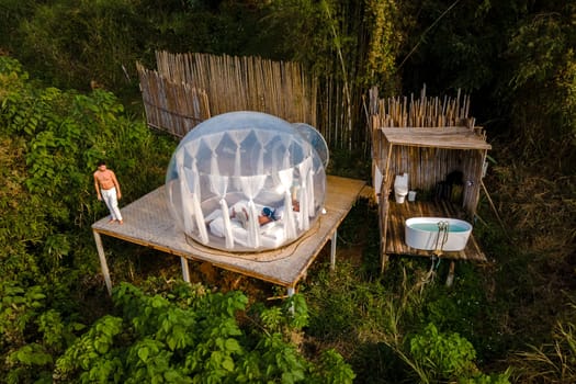 couple man and women in a bubble tent with an outdoor bathroom with a bath in the jungle rainforest. Luxury glamping