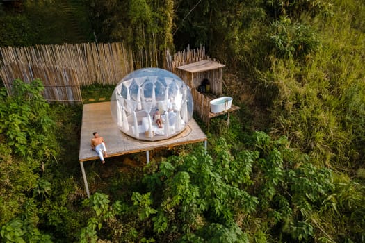 couple man and women in a bubble tent with an outdoor bathroom with a bath in the jungle rainforest. Luxury glamping in Thailand