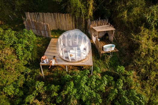 couple man and women in a bubble tent with an outdoor bathroom with a bath in the jungle rainforest. Luxury glamping in Thailand