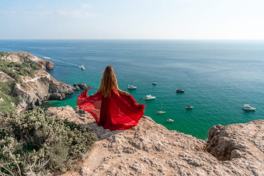 Woman sea red dress yachts. A beautiful woman in a red dress poses on a cliff overlooking the sea on a sunny day. Boats and yachts dot the background