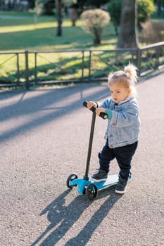 Little girl stands with a scooter on the road, thinking. High quality photo