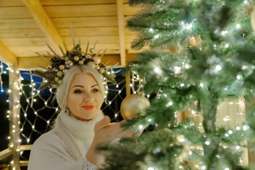 Happy blonde as Snow Maiden in white costume. Wooden house exterior Festive setting. Character with crown creating festive scene