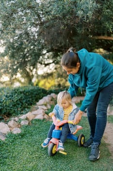 Mom teaches a little girl to pedal a bicycle on the lawn. High quality photo