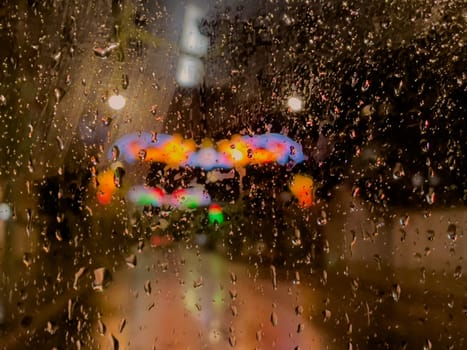 Rain bokeh road lights. Abstract shot of evening city traffic bokeh. Multicolored lights of the evening city and passing cars through a wet rainy window
