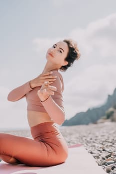 Young woman with long hair in white swimsuit and boho style braclets practicing outdoors on yoga mat by the sea on a sunset. Women's yoga fitness routine. Healthy lifestyle, harmony and meditation