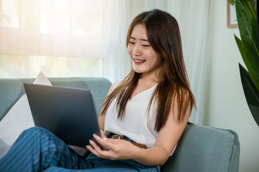 Happy woman browsing through the internet during free time on laptop computer, Female smiling sit on sofa using laptop in living room at home, girl shopping or chatting online in social media network