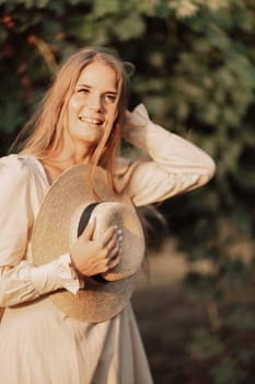 Woman with straw hat stands in front of vineyard. She is wearing a light dress and posing for a photo. Travel concept to different countries.