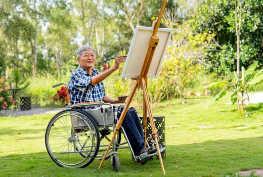 Front view of Asian senior man sit on wheelchair and paint the painting outdoor for relax and revive good health of old people outside.