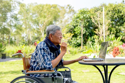 Asian senior man take off the eyeglasses to look more clearly for watching the laptop outdoor in the garden.