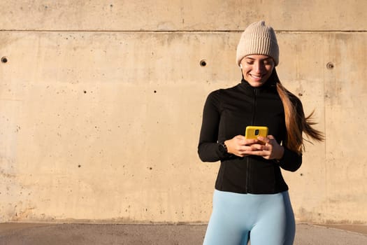 Young happy woman using phone after winter workout outdoors. Copy space. Lifestyle and technology concepts.