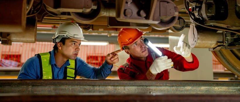 Wide image of engineer and technician workers check and maintenance under the train with use light tube to support in train factory workplace.