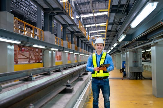 Professional engineer worker hold tablet and look at camera with smiling also stand near railroad tracks in factory workplace.