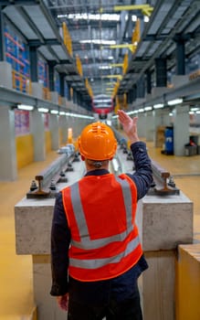 Vertical image back of technician worker with safety uniform show body signal to electrical or metro train and stand in front of railroad tracks in factory workplace.