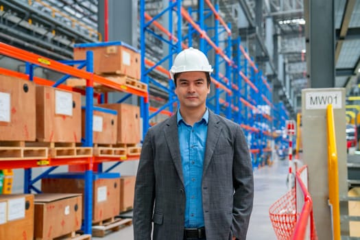 Portrait of professional engineer worker hold tablet and look at camera also stand in front of product shelves in factory or warehouse workplace.