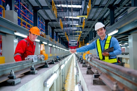 Professional engineer look and camera also hold tablet and point to technician worker near railroad tracks of electrical or sky train in factory workplace.