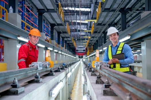 Professional engineer hold tablet and stand with technician worker near railroad tracks of electrical or sky train in factory workplace also look at camera with smiling.