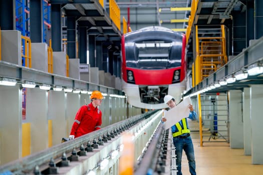 Professional engineer show the detail in plan or drawing document to technician worker to check the problema of railroad tracks of electrical or sky train in factory workplace.