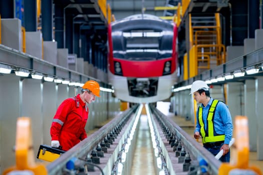 Professional engineer and technician workers discuss and stay in front of train to check function of railroad tracks of electrical or sky train in factory workplace.