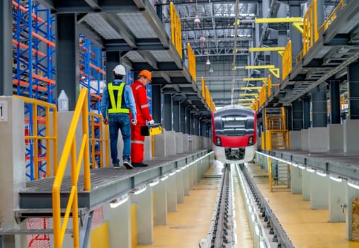 Wide shot professional engineer and technician workers walk beside railroad tracks of electrical or sky train in factory workplace and go to check and maintenance the train.