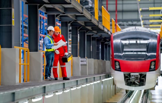 Professional engineer hold drawing plan and technician worker stay and discuss beside railroad tracks of electrical or sky train in factory workplace.