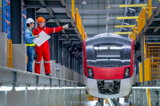 Professional technician point to right direction and discuss with engineer near railroad tracks of electrical or sky train in factory workplace.