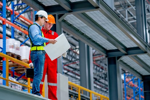 Professional engineer hold drawing plan and technician worker stay and discuss beside railroad tracks in the factory.