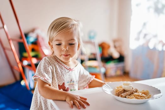 Little girl stands near the table in front of a plate of breakfast and looks away. High quality photo