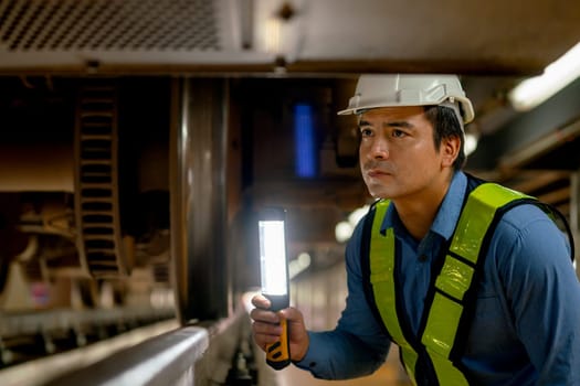 Professional engineer worker check and maintenance under the train with use light tube to support in train factory workplace.