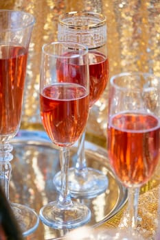 alcohol drinks concept. glasses of rose champagne and bottle on the tray on sparkling golden tablecloth