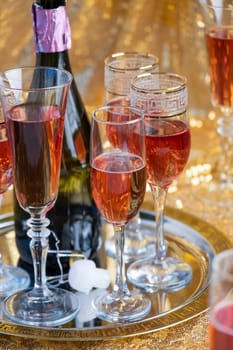 alcohol drinks concept. glasses of rose champagne and bottle on the tray on sparkling golden tablecloth