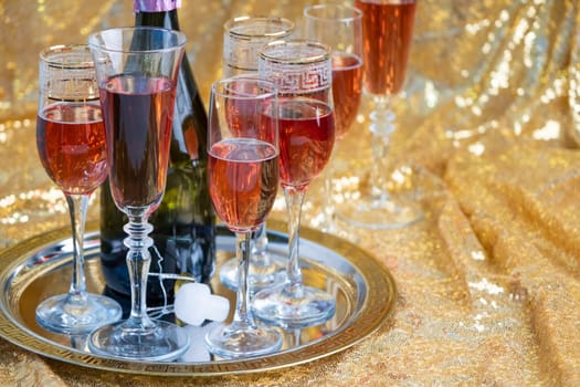 alcohol drinks concept. glasses of rose champagne and bottle on the tray on sparkling golden tablecloth